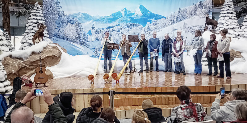 Winterdekoration im Allee-Center-Leipzig mit Alphornbläsern vor Großformartdruck mit Berglandschaft