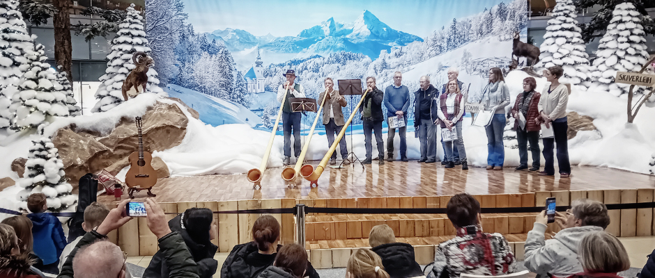 Winterdekoration im Allee-Center-Leipzig mit Alphornbläsern vor Großformartdruck mit Berglandschaft